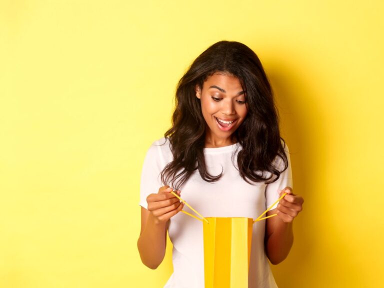 A delighted young woman peeks into an empty yellow shopping bag